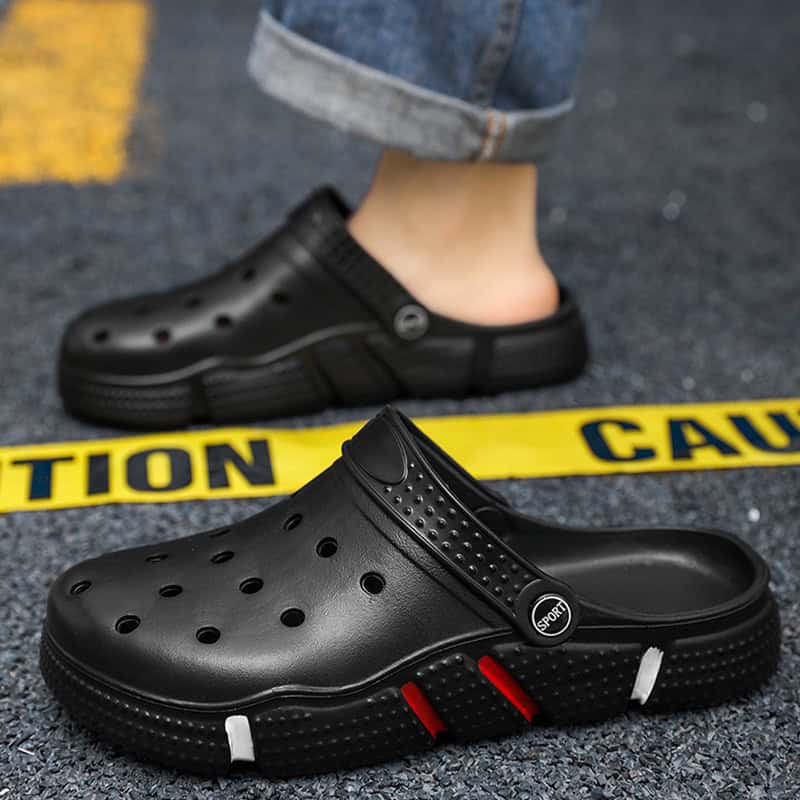 lightweight-eva-slides-black-clog-sandal-non-slip-mules Safety footwear, caution tape, and person in jeans on asphalt surface.